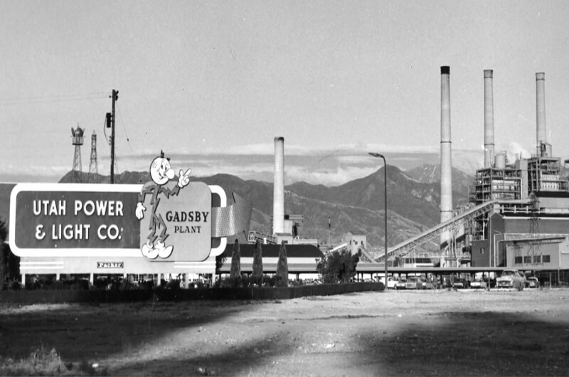 Imagen en blanco y negro de la Planta Gadsby de Utah Power & Light Co. con chimeneas, edificios industriales y montañas al fondo cerca del río Jordan de North Temple, un sitio que ahora se considera para desarrollo listo para iniciar en Utah.