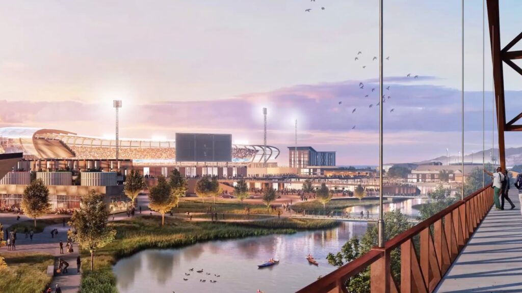 Una vista de un estadio moderno, preparado para la expansión de la MLB en Salt Lake City, con luces encendidas junto al río Jordan de North Temple; personas caminan por el puente al atardecer mientras kayaks navegan por el río, todo dentro de un desarrollo de uso mixto totalmente eléctrico rodeado de árboles y agua.
