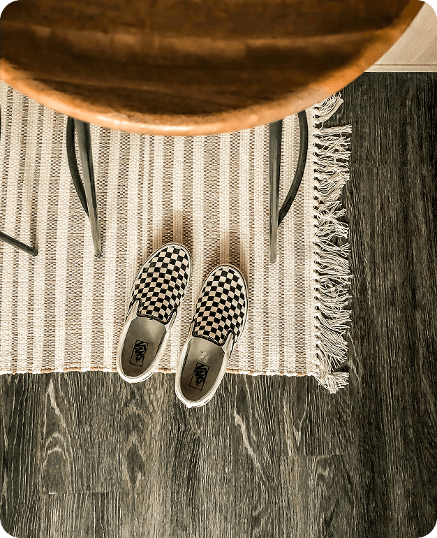 A pair of black and white checkered slip-on shoes on a striped rug next to a wooden chair on the dark wood floor, inspired by the vibrant style found in Salt Lake westside business district near North Temple Jordan River.