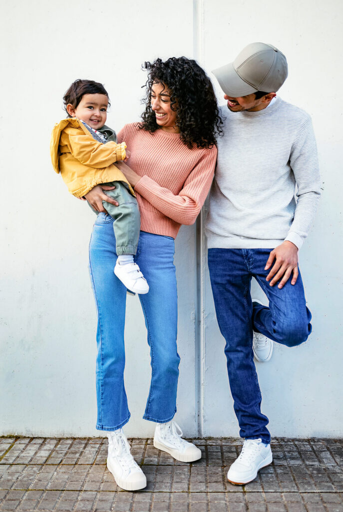 A woman holds a young child while standing next to a man, all smiling and dressed casually against a plain light-colored wall—capturing the spirit of community found in Utah’s shovel-ready developments.